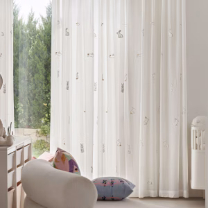 Detail van een witte vitrage met schattige konijntjes naast een babybed in een kinderkamer