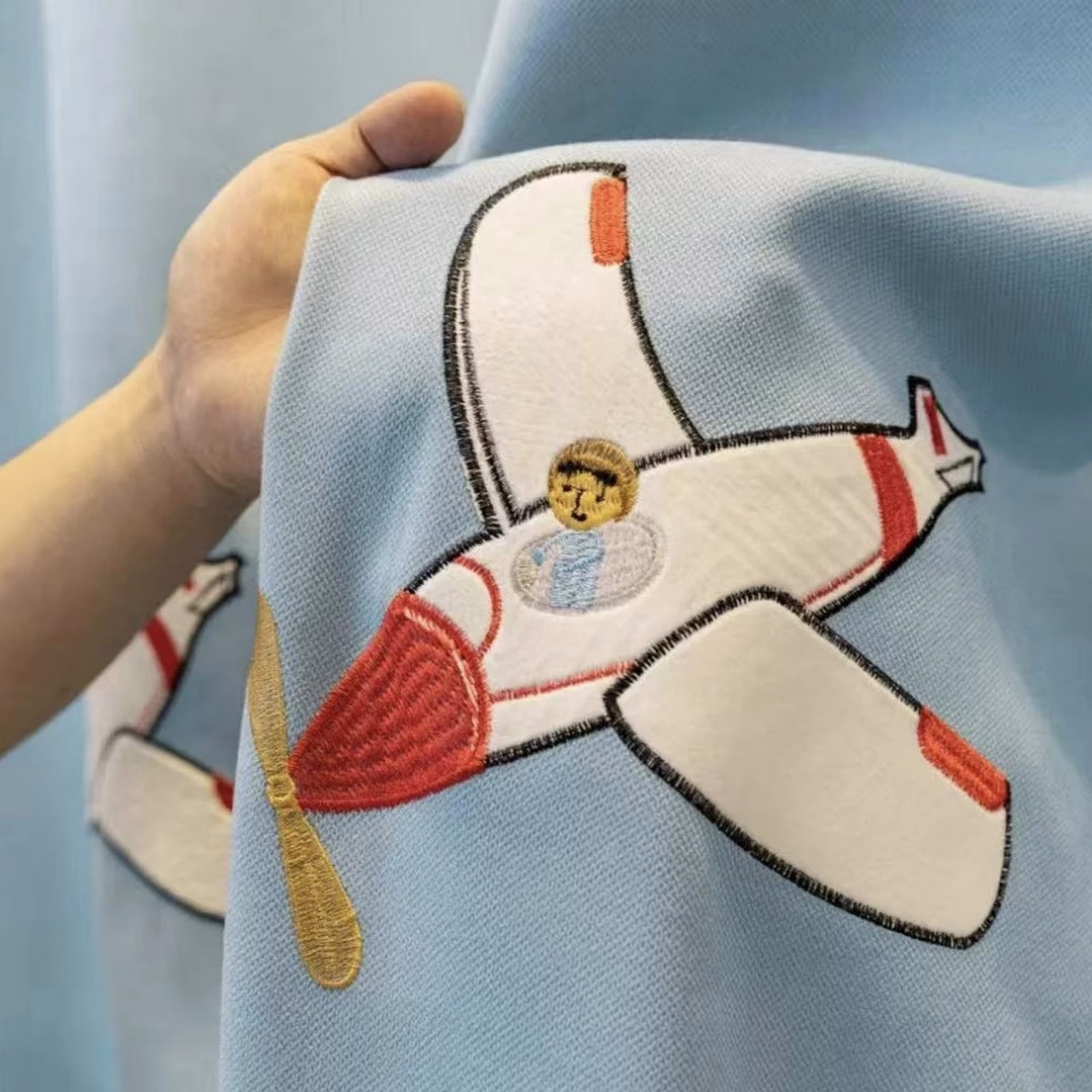Detail van geborduurd vliegtuig op lichtblauw kindergordijn